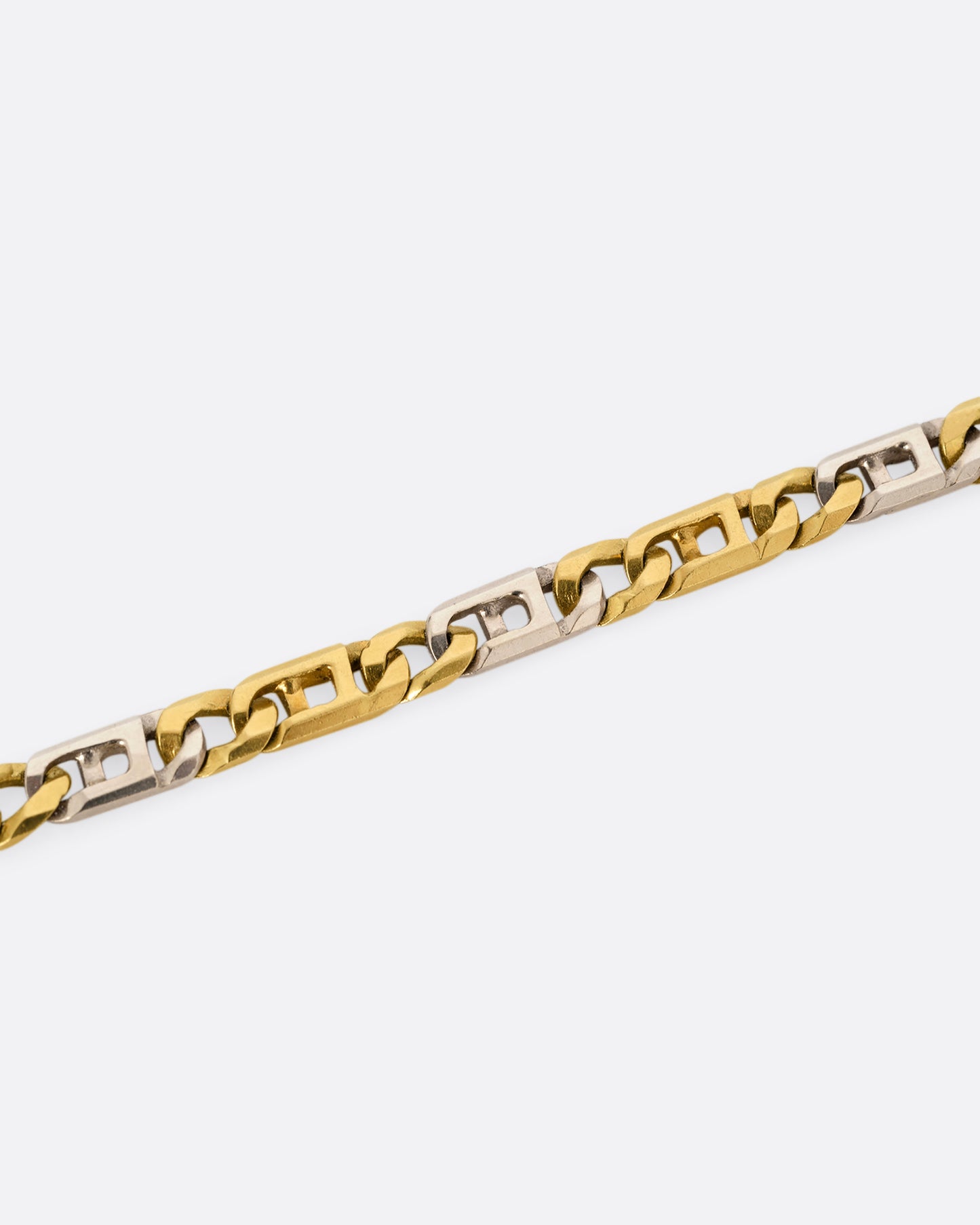 A white and yellow gold geometric flat chain necklace. Shown close up on the links.