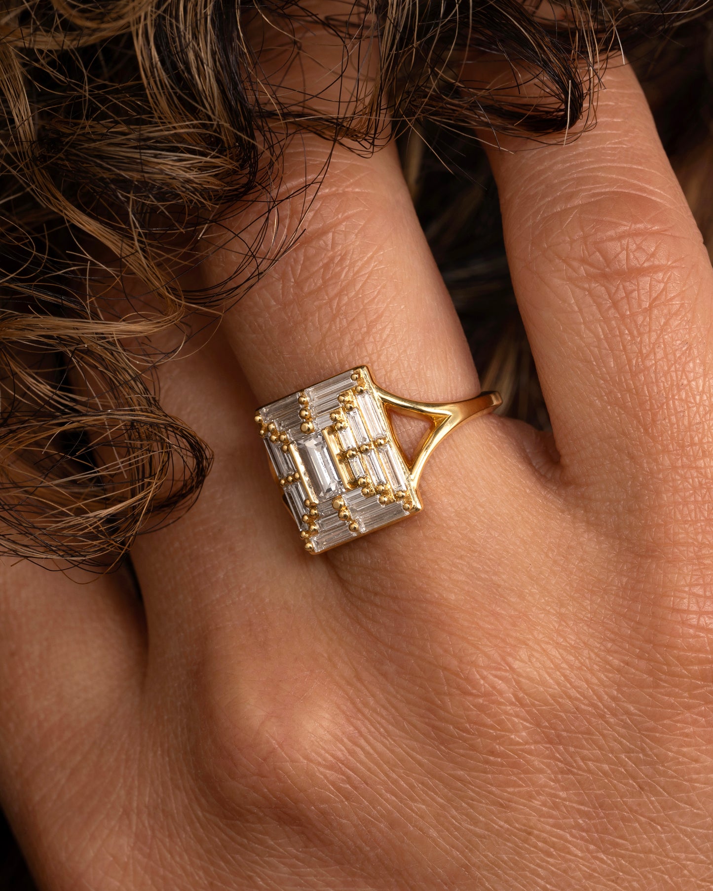 A yellow gold ring with a mosaic of white diamonds in the shape of a square. Shown worn on a hand.