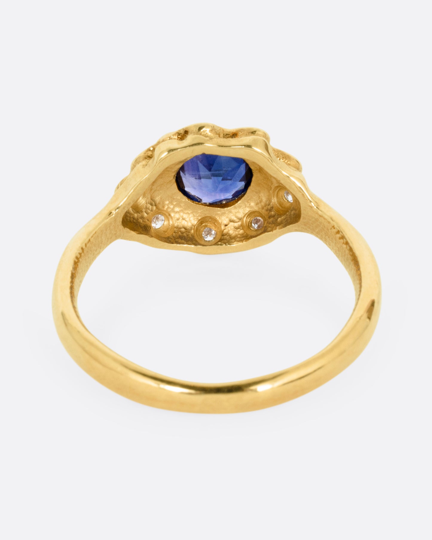 A yellow gold ring with a halo of white diamonds around a sapphire, shown from the back.