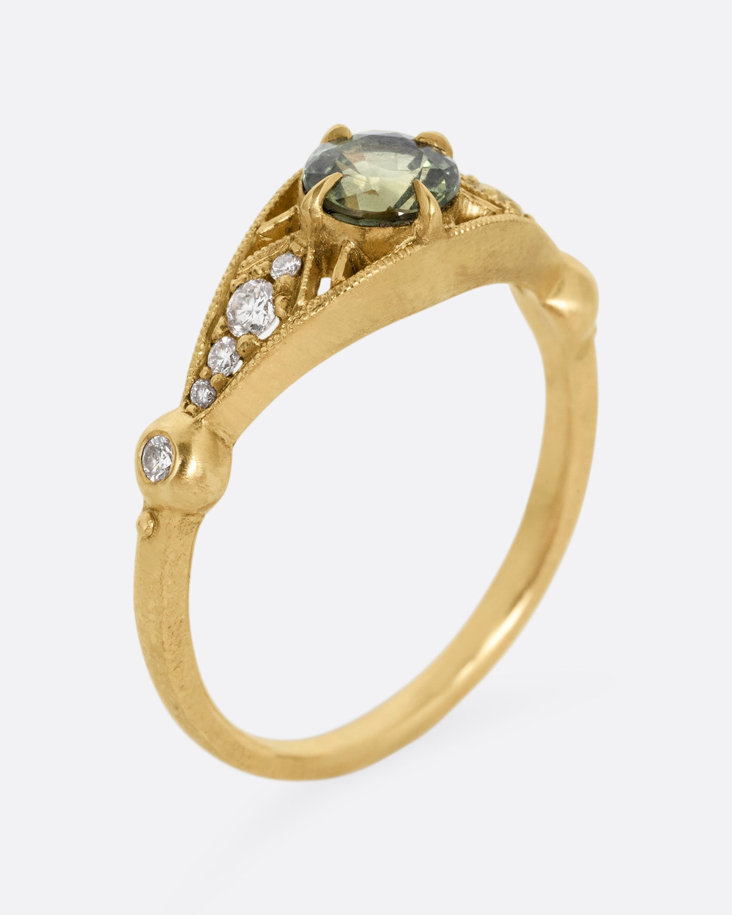 A yellow gold ring with a green Montana sapphire at the center and cutout details and white diamonds. Shown standing up from the side.