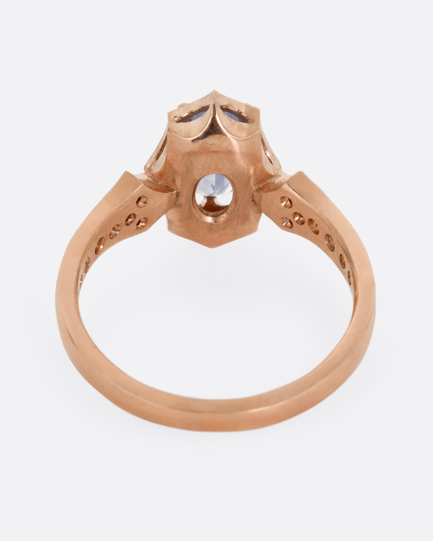 A rose gold ring with a prong set lavender sapphire at the center and diamond lined shoulders. Shown from the back.