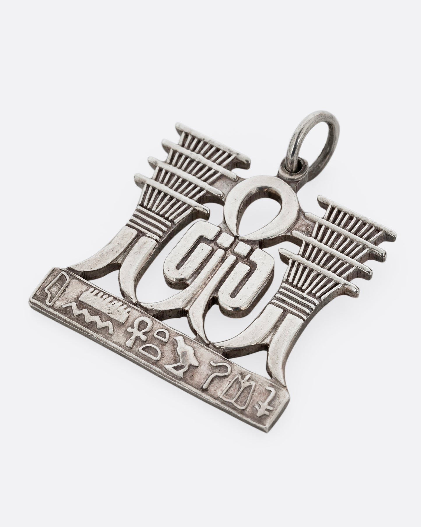 A silver pendant with Egyptian symbols of Sa and Djed with hieroglyphs along the bottom. Shown from the front lying flat.