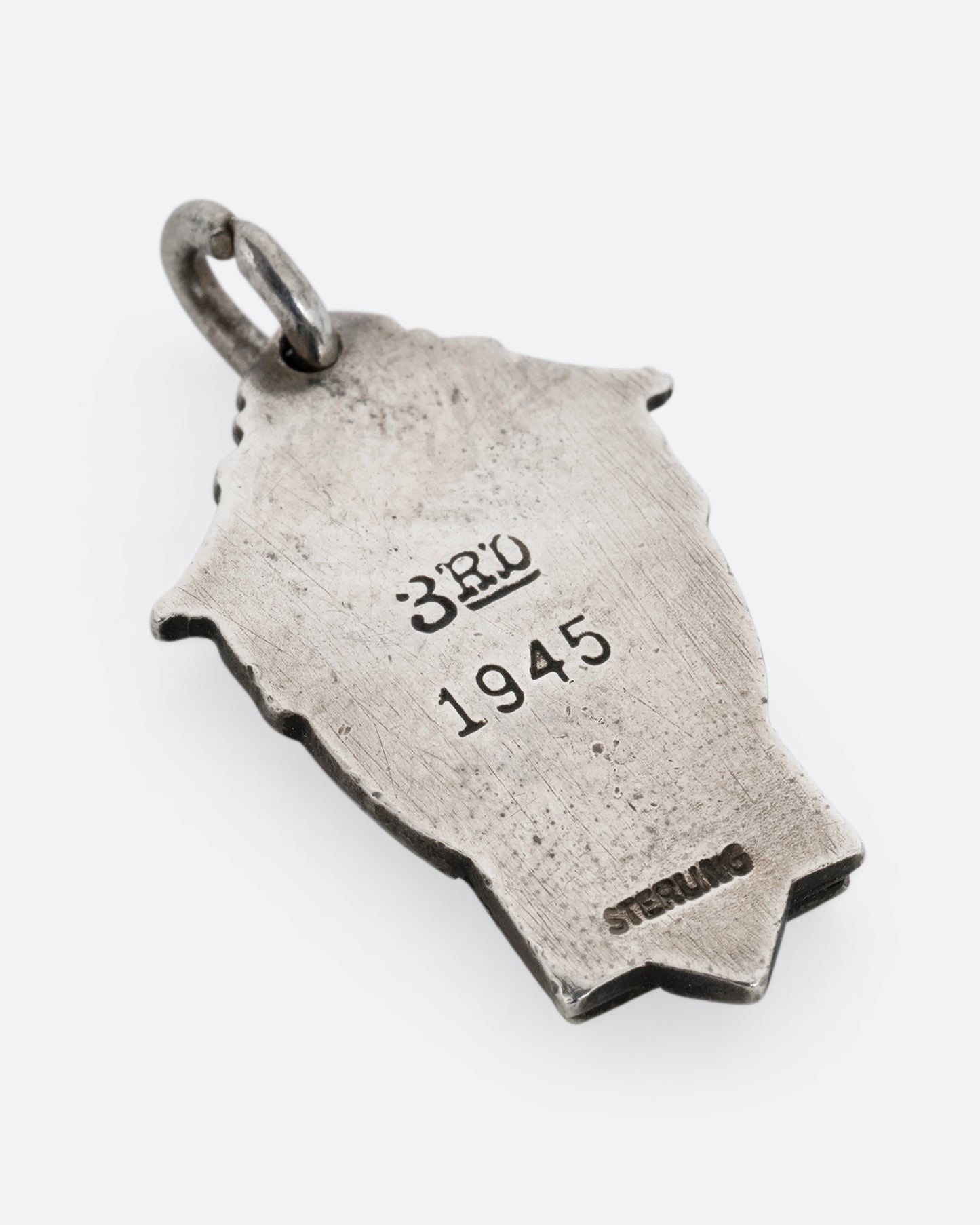A silver crest shaped pendant with '3rd 1945'. Shown from the back.