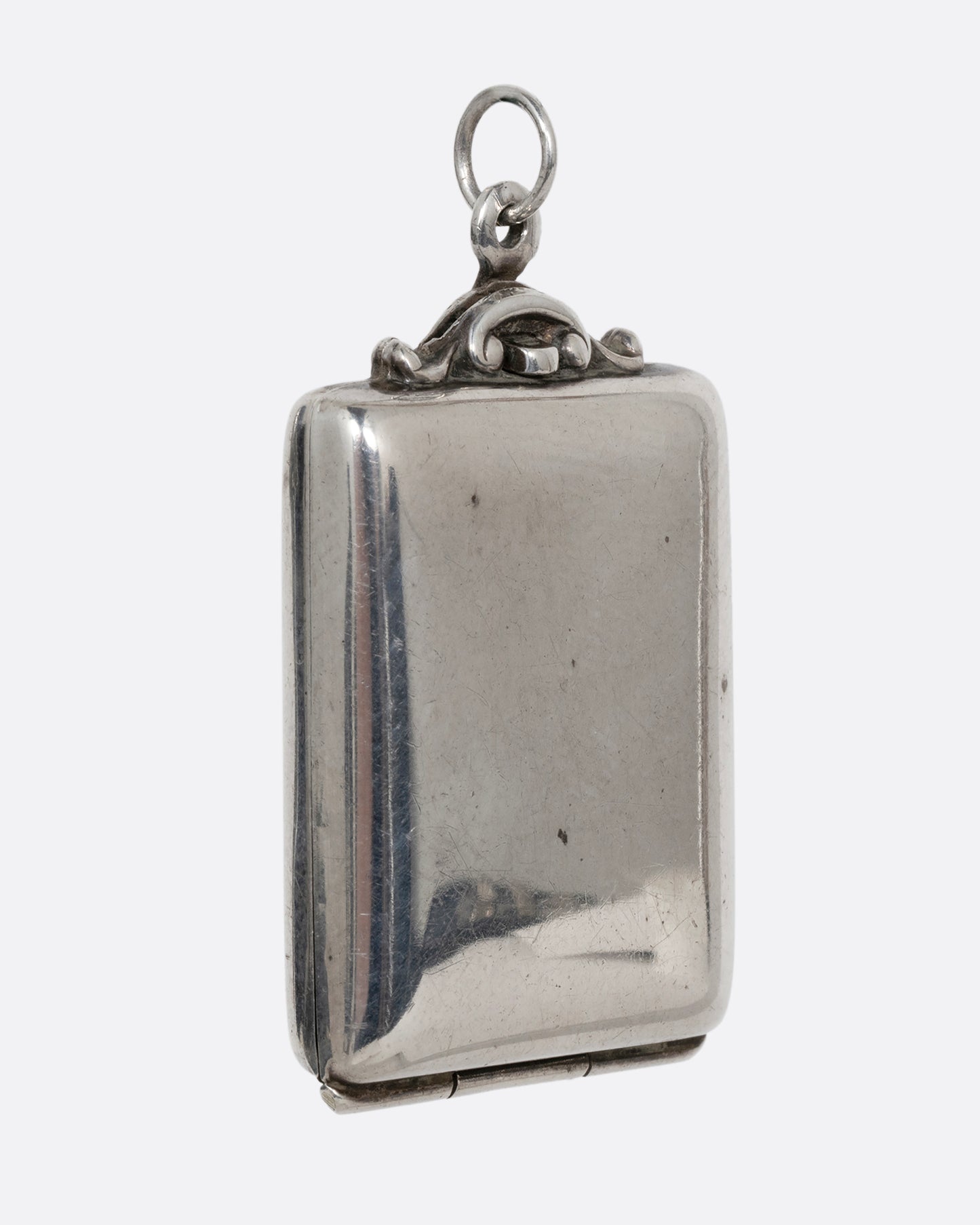 A silver rectangular locket with a filigreed top and hinged bottom. Shown from the side.