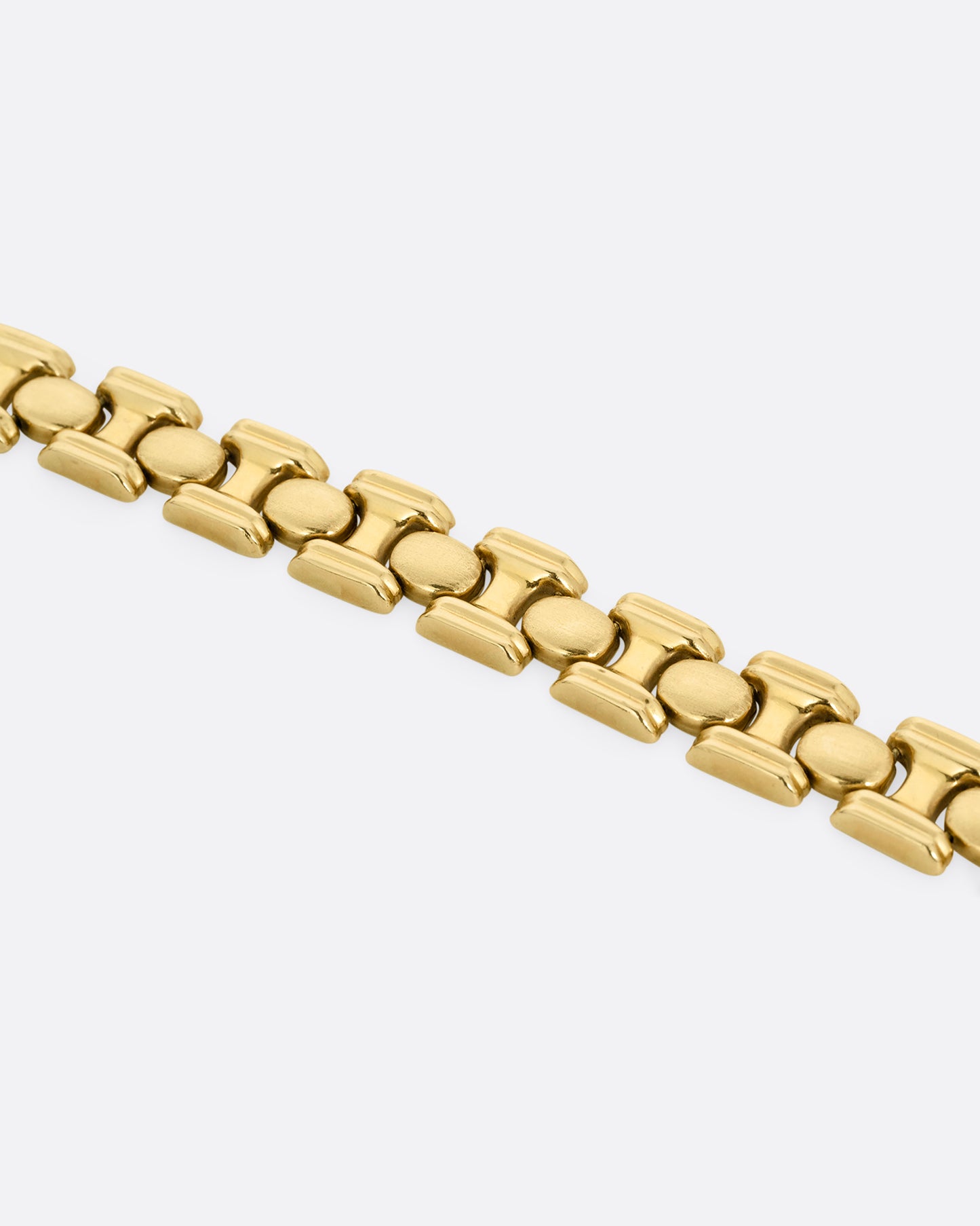 A close up of a yellow gold bracelet with repeating oval sections. Shown open and lying flat.