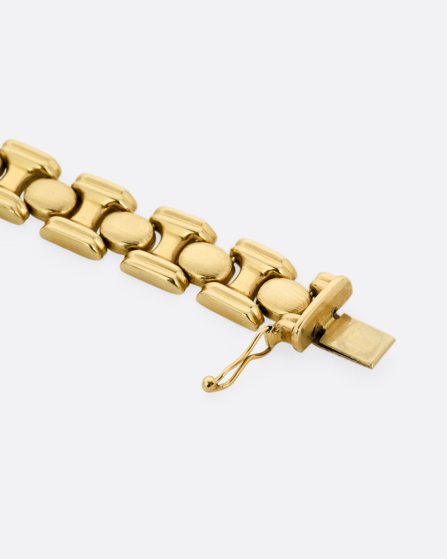 A close up of the clasp on a yellow gold bracelet with repeating oval sections. Shown open and lying flat.