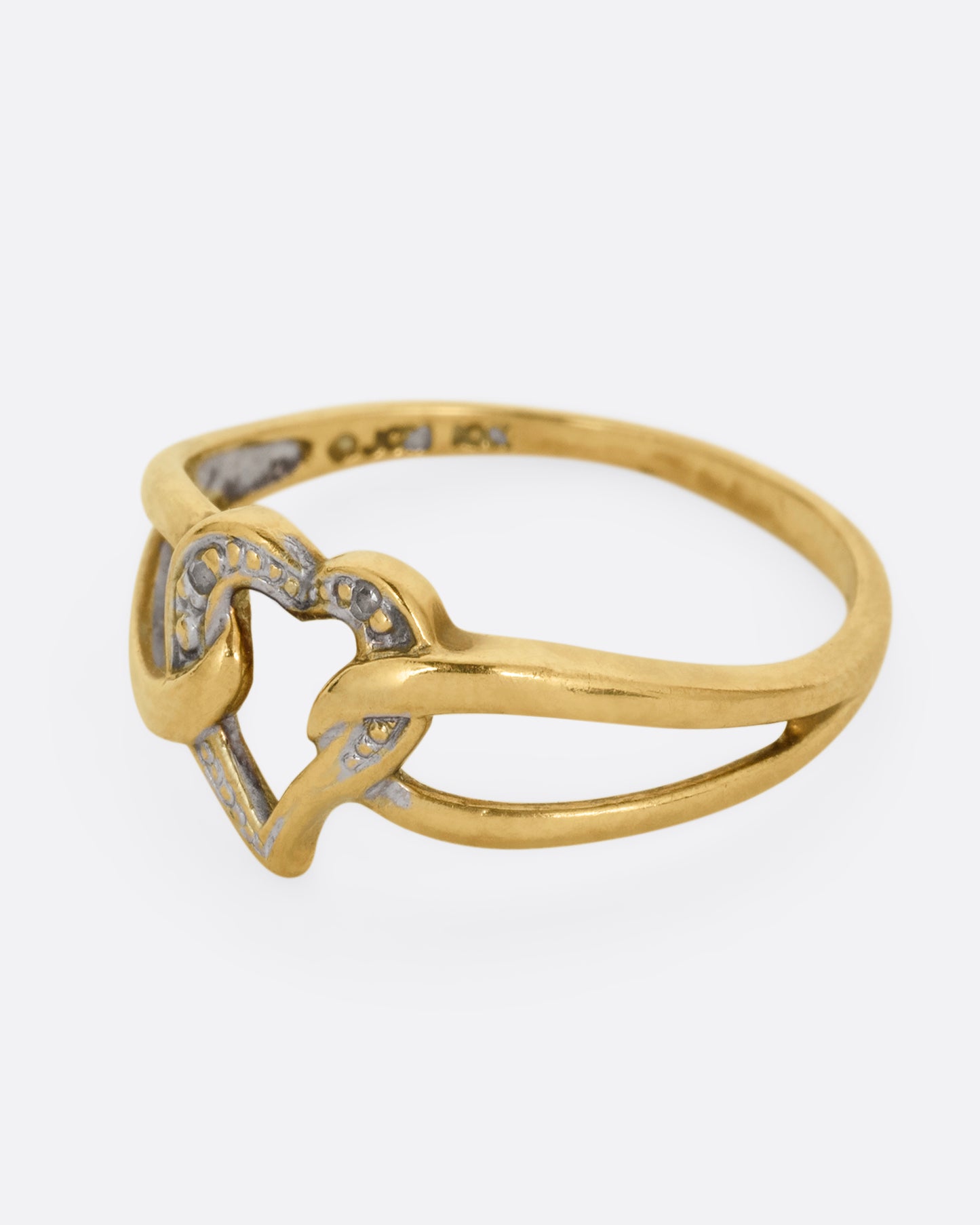 A yellow and white gold ring with an open heart and looped shoulders. Shown from the side.