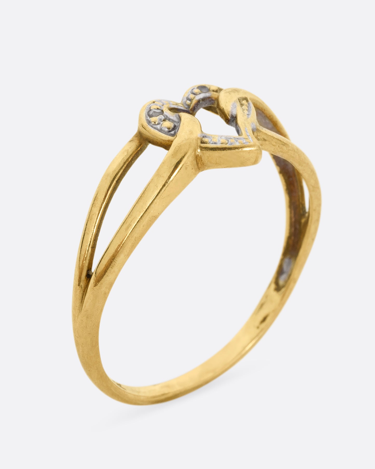 A yellow and white gold ring with an open heart and looped shoulders. Shown standing up from the side.