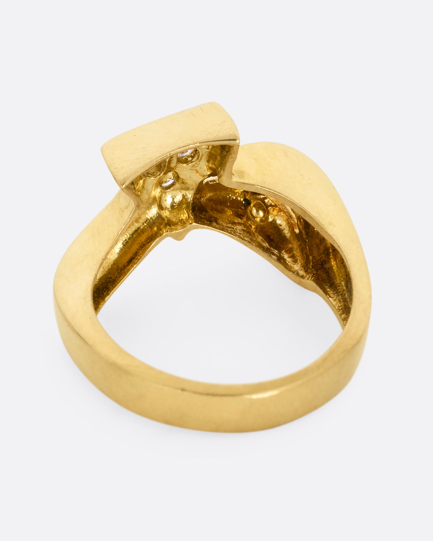A yellow gold ring with a curvy band and three diamonds set in a triangular shaped setting. Shown from the back.