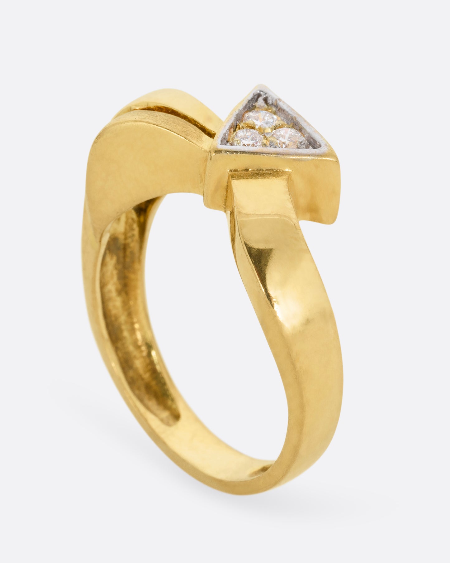A yellow gold ring with a curvy band and three diamonds set in a triangular shaped setting. Shown standing up from the side.