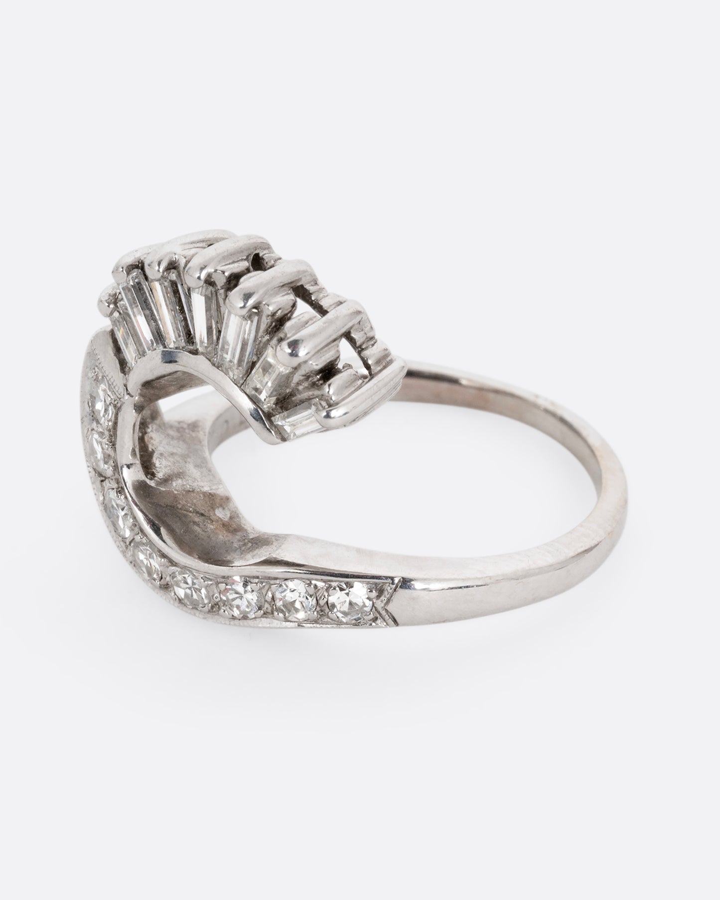 A white gold wave ring with baguette diamonds and round diamonds. Shown from the side.