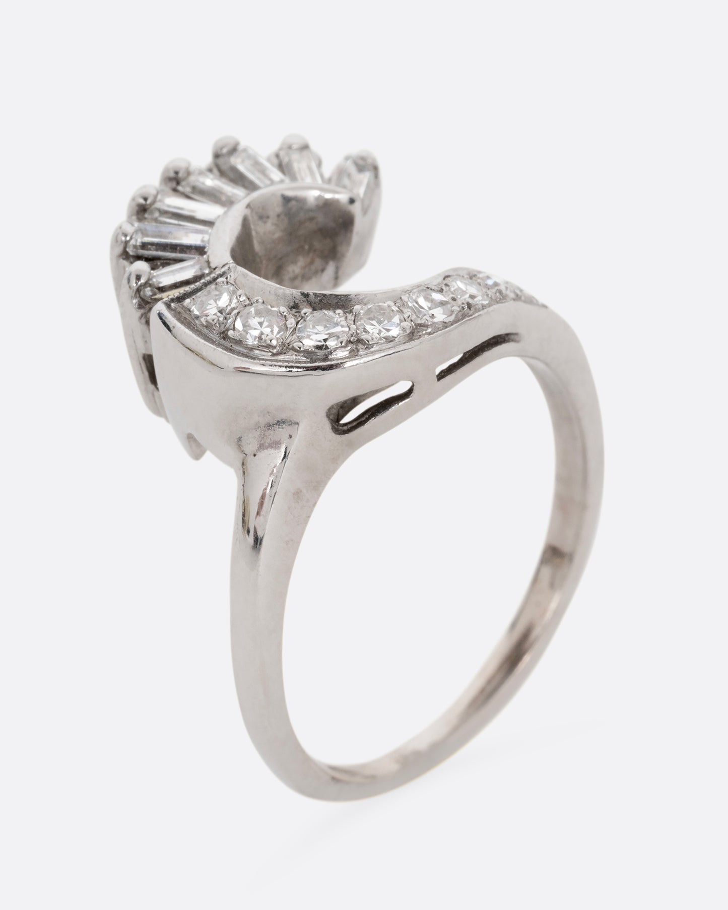 A white gold wave ring with baguette diamonds and round diamonds. Shown standing up diagonally from the front.