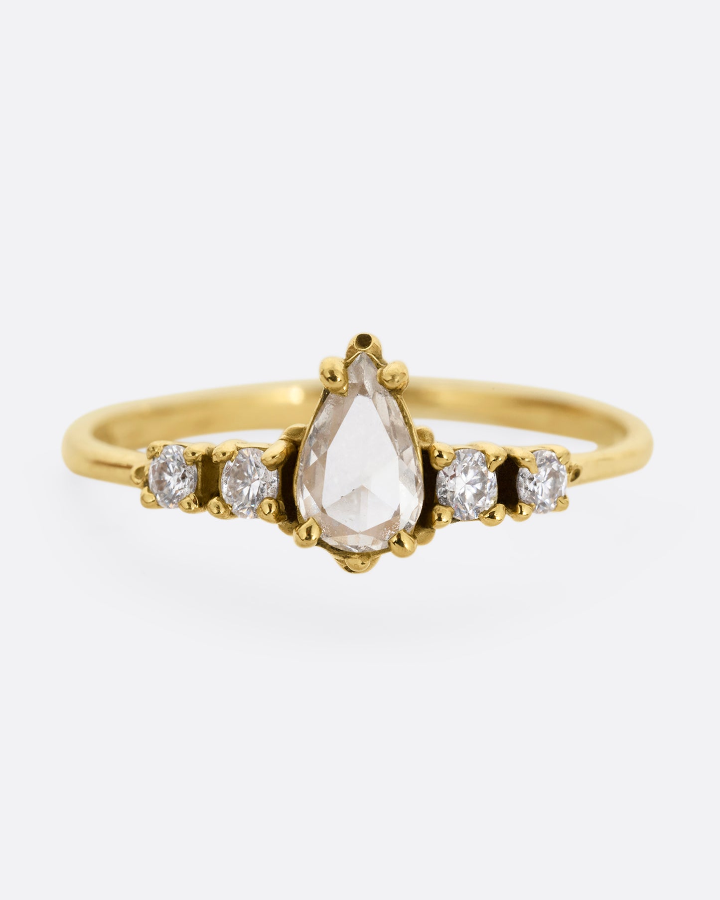 A yellow gold ring with a pear shaped champagne diamond with round white diamond accents. Shown from the front.
