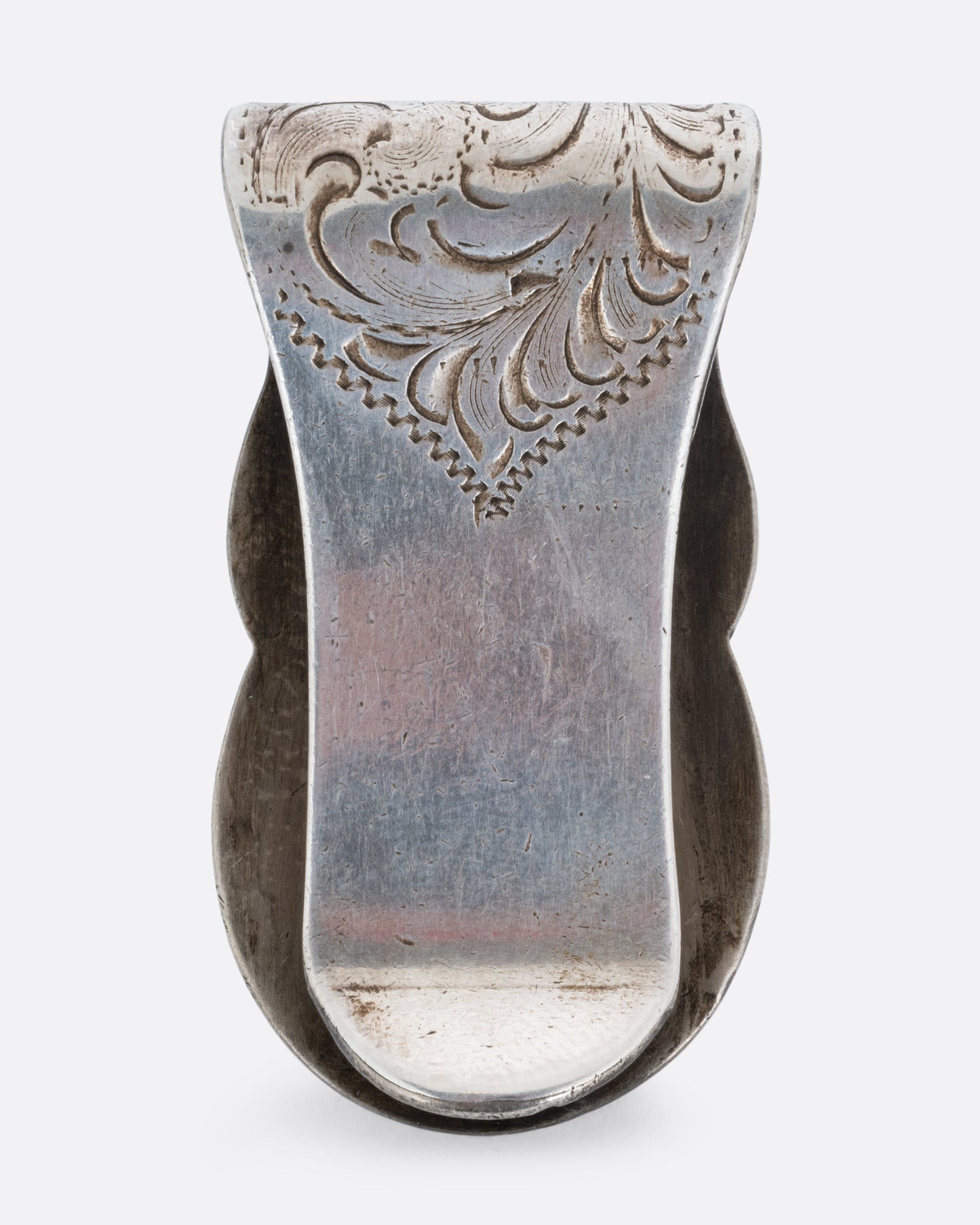 A silver money clip with a swirling engraved pattern shown from the back.
