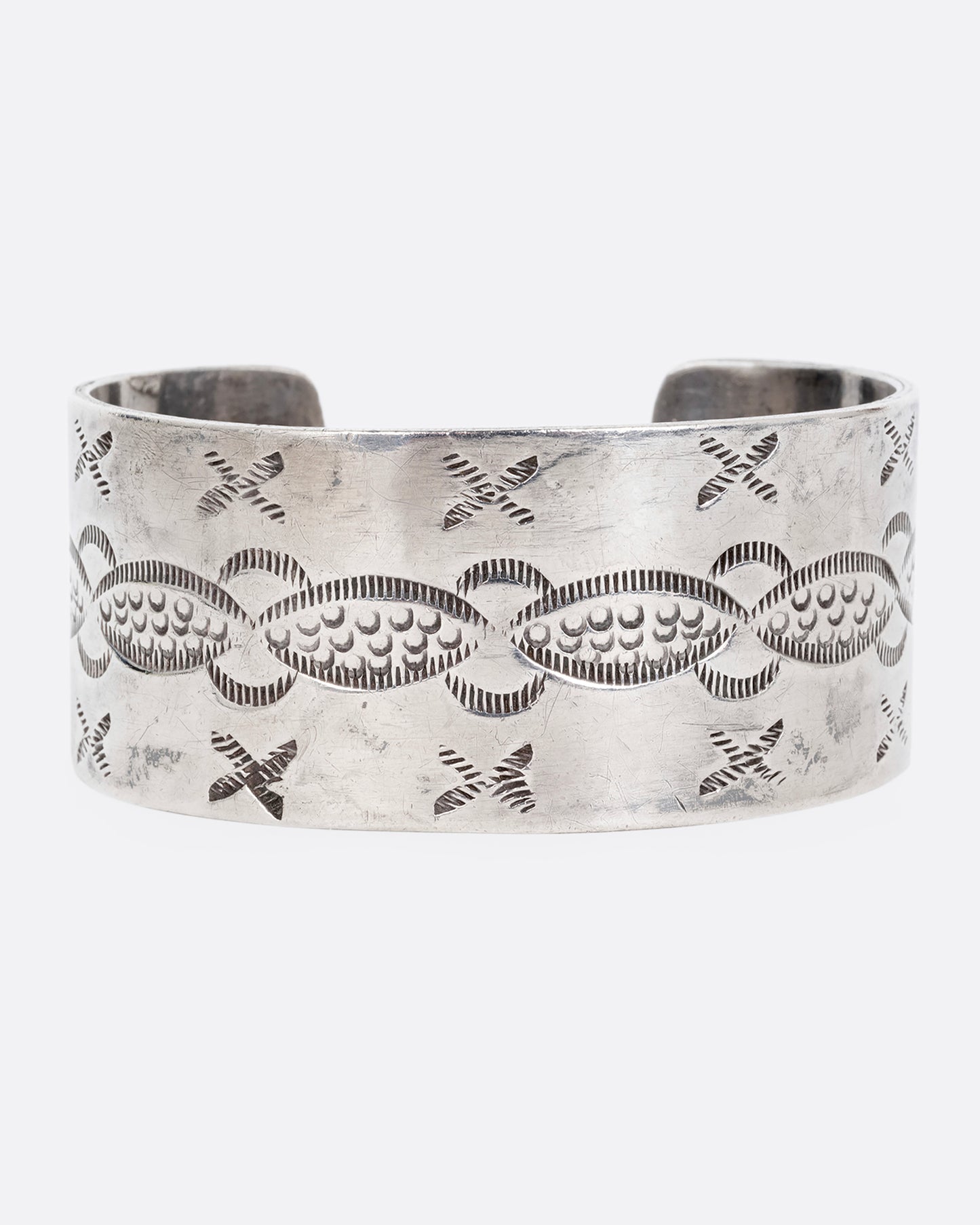 A wide silver cuff bracelet with stamping. Shown on its side from the front.
