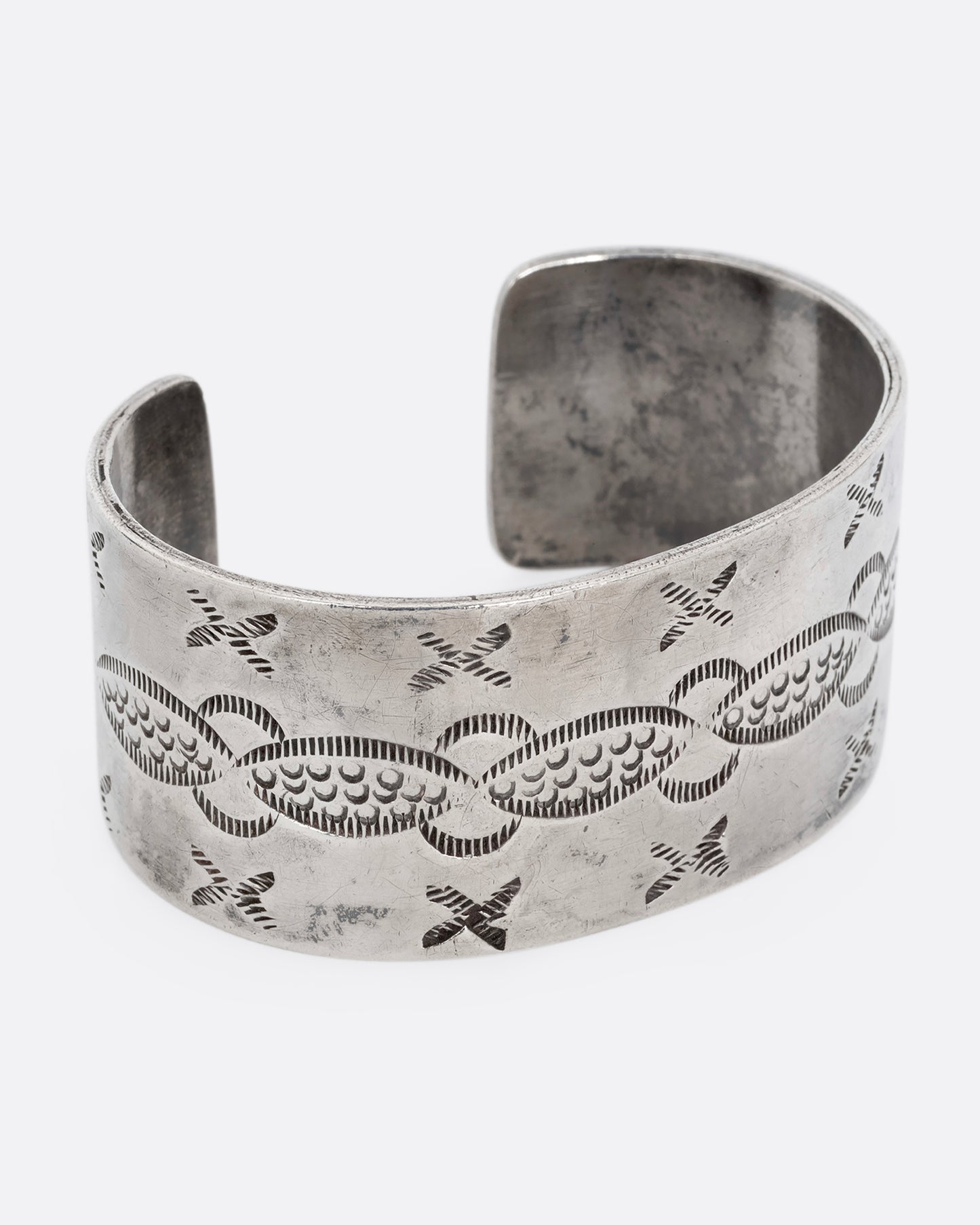 A wide silver cuff bracelet with stamping. Shown from the side.