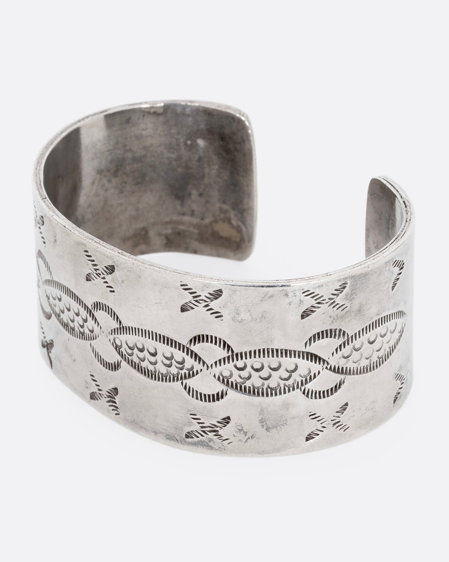 A wide silver cuff bracelet with stamping. Shown from the side.