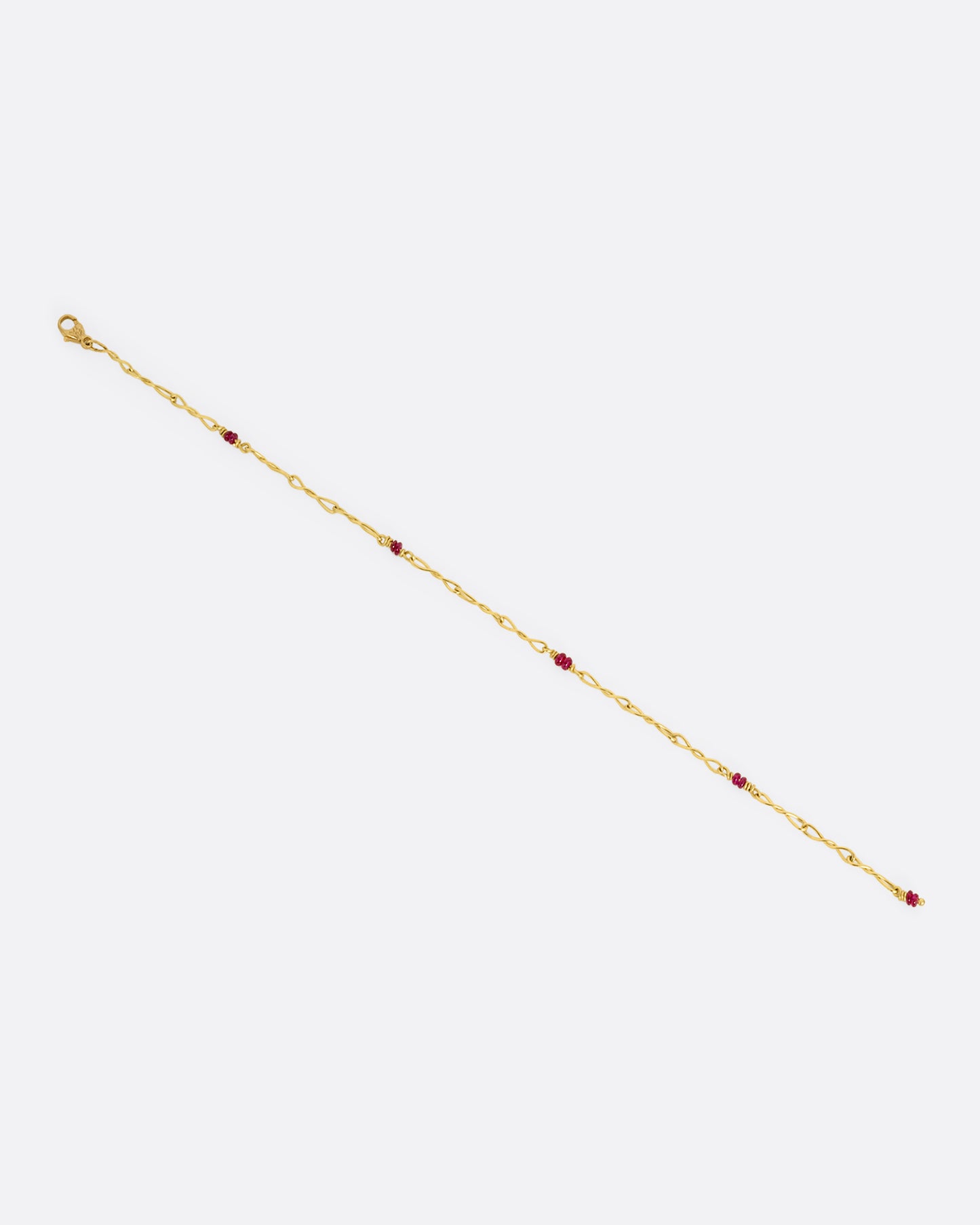 A yellow gold twisted paperclip chain link bracelet with five ruby beads.Shown lying flat unclasped.