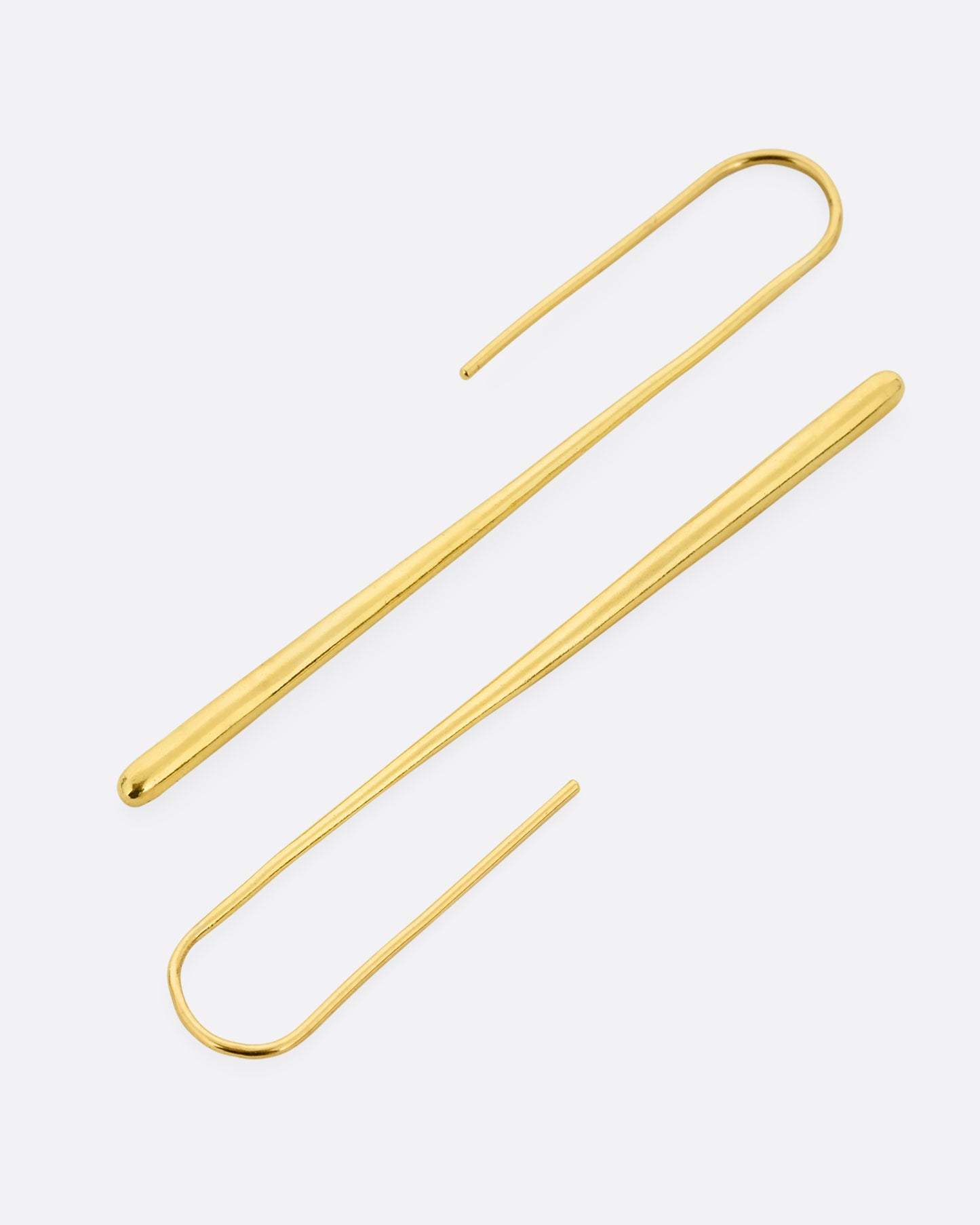 A pair of long narrow yellow gold earrings with a tapered silhouette and ear hooks. One earring is shown on its side from the bottom. The other earring is shown lying on its from the top.