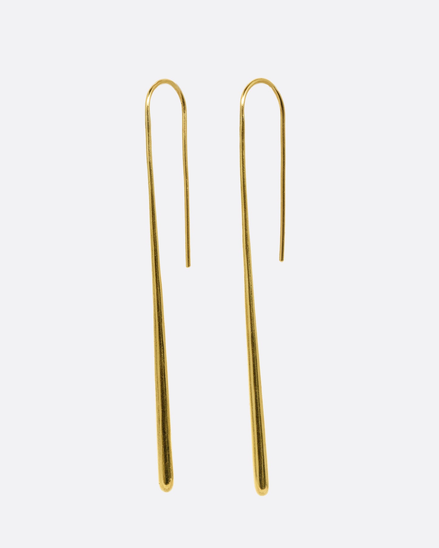 A pair of long narrow yellow gold earrings with a tapered silhouette and ear hooks. Shown from the side.