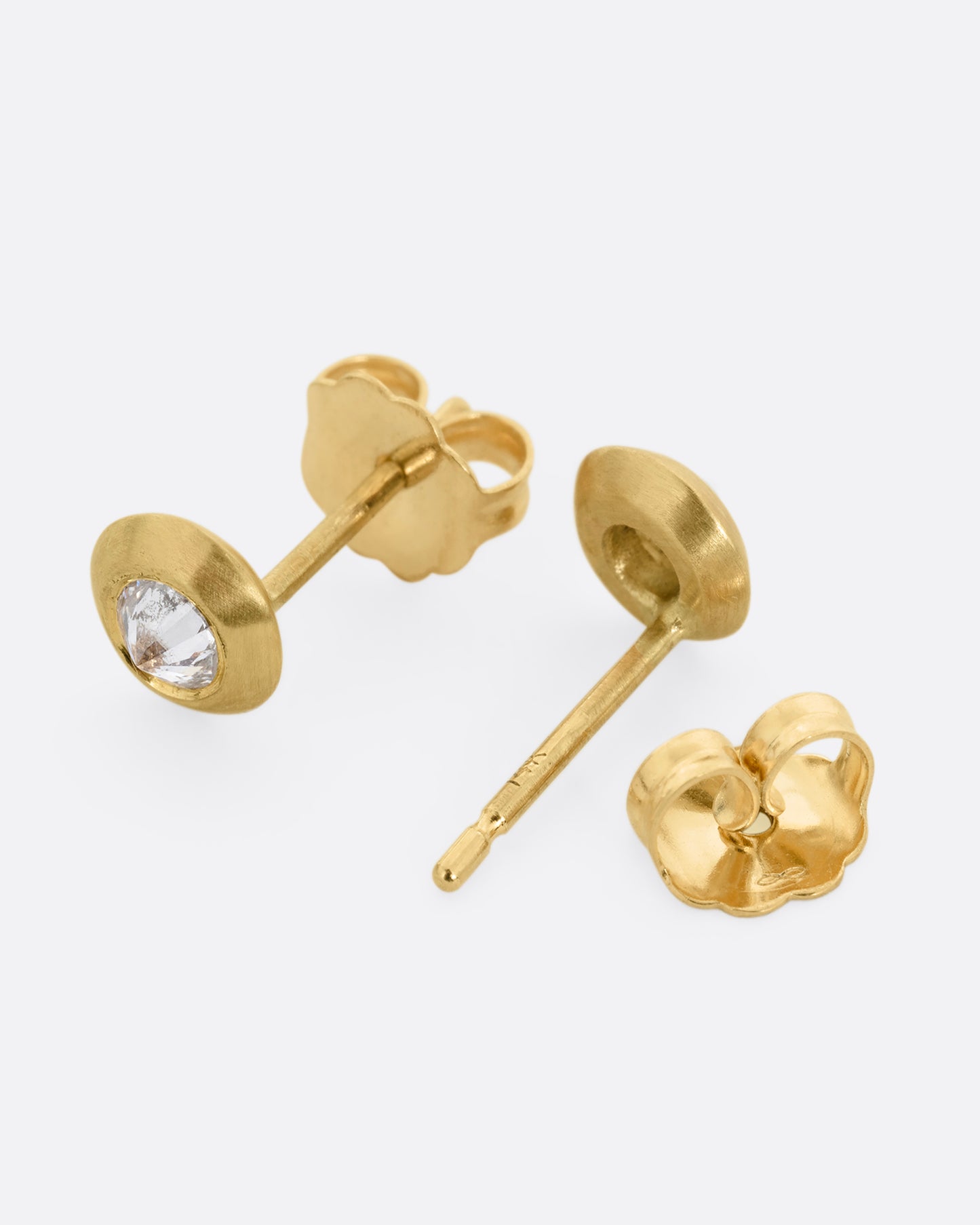 Reverse set diamond stud earrings in yellow gold. One earring is shown lying flat diagonally from the front. The other earring is shown open lying flat from the back.