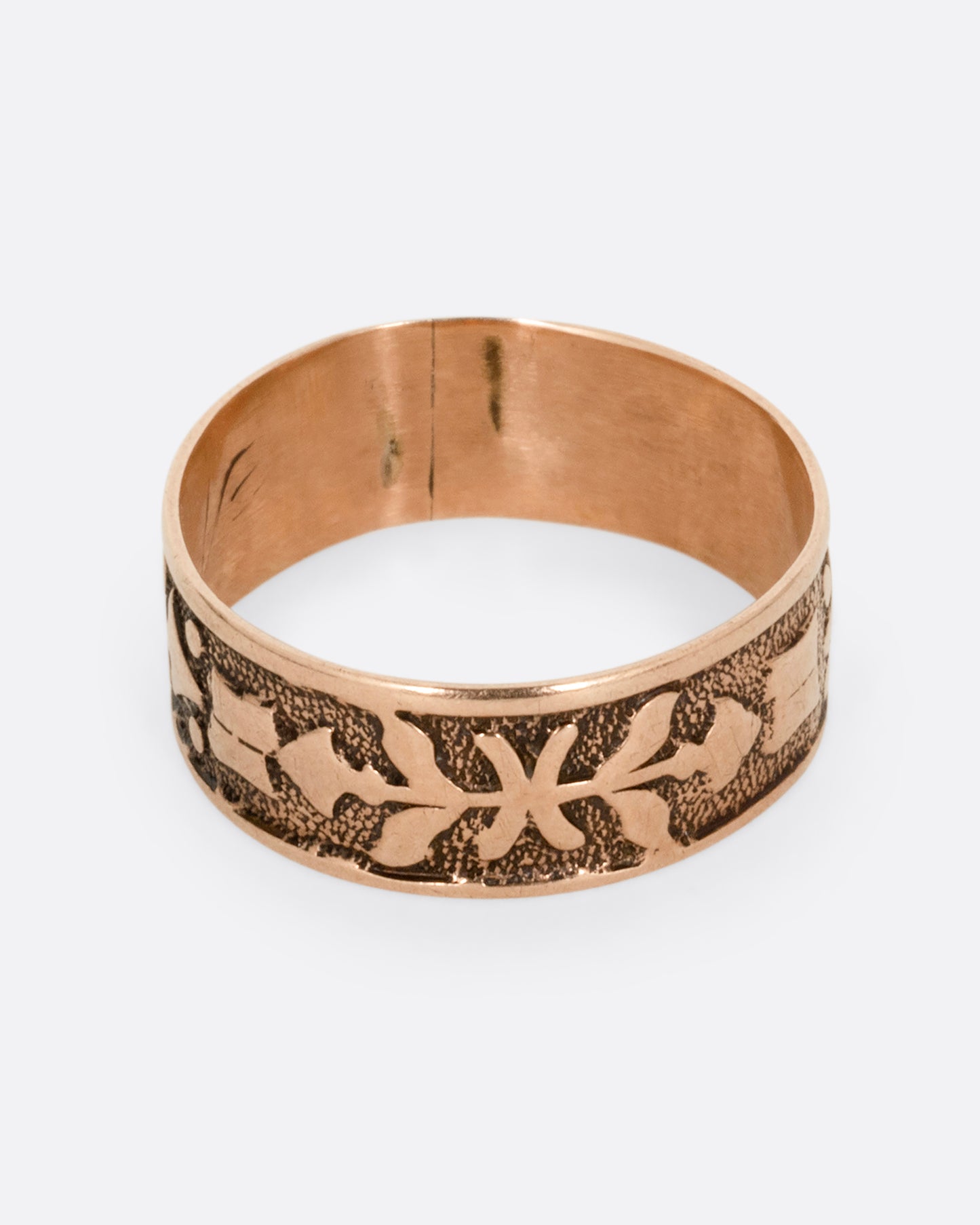 A rose gold cigar band with stamped arrow motif. Shown from the top.
