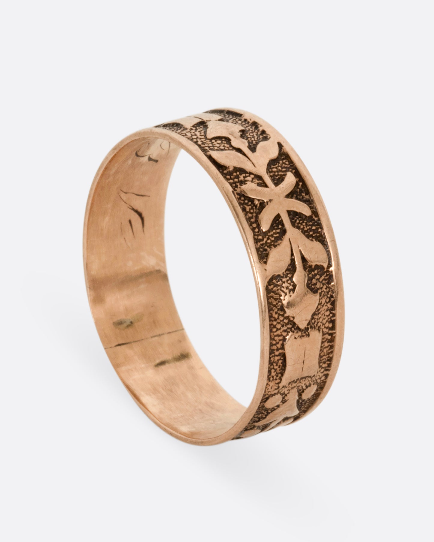 A rose gold cigar band with stamped arrow motif. Shown standing up from the side.