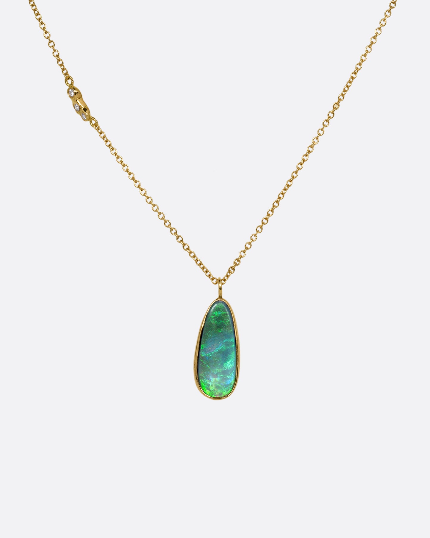 An opal pendant set in yellow gold hanging from a yellow gold cable chain with diamond details on one side of the chain. Shown from the front.