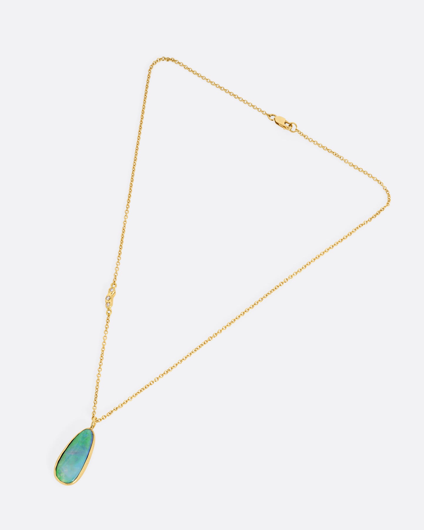 An opal pendant set in yellow gold hanging from a yellow gold cable chain with diamond details on one side of the chain. Shown lying flat closed from the front.