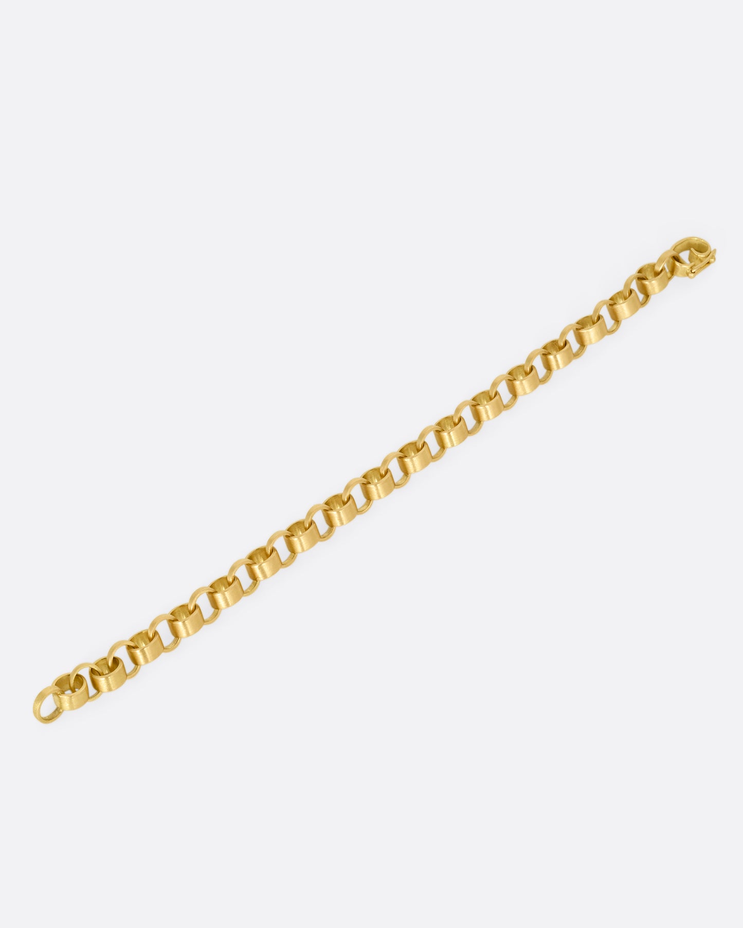 A yellow gold bracelet with bicycle chain inspired links. Shown open lying flat from the side.