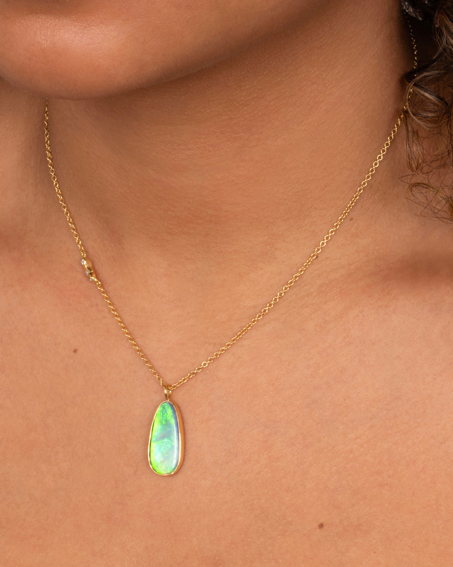 An opal pendant set in yellow gold hanging from a yellow gold cable chain with diamond details on one side of the chain. Shown from the front on a person.