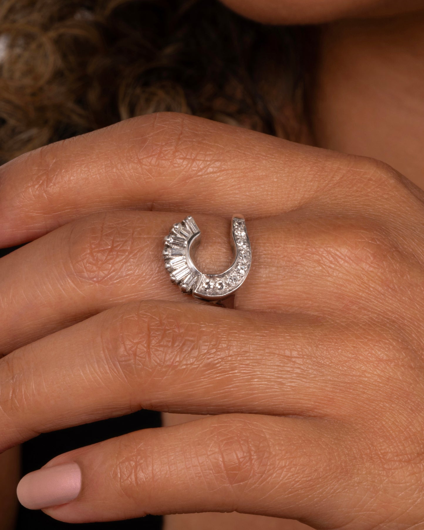 A white gold wave ring with baguette diamonds and round diamonds. Shown on a hand from the front.