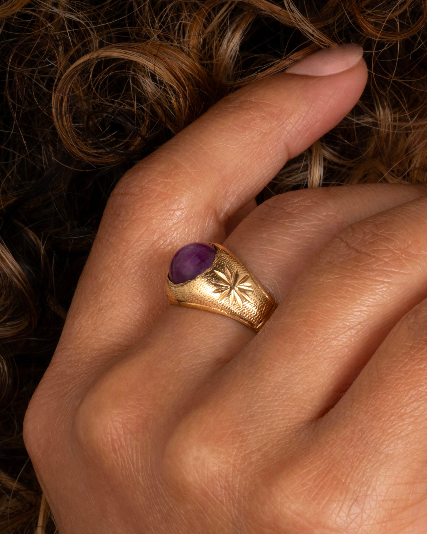A domed yellow gold vintage ring with a ruby cabochon and starflower details. Shown worn on a finger.