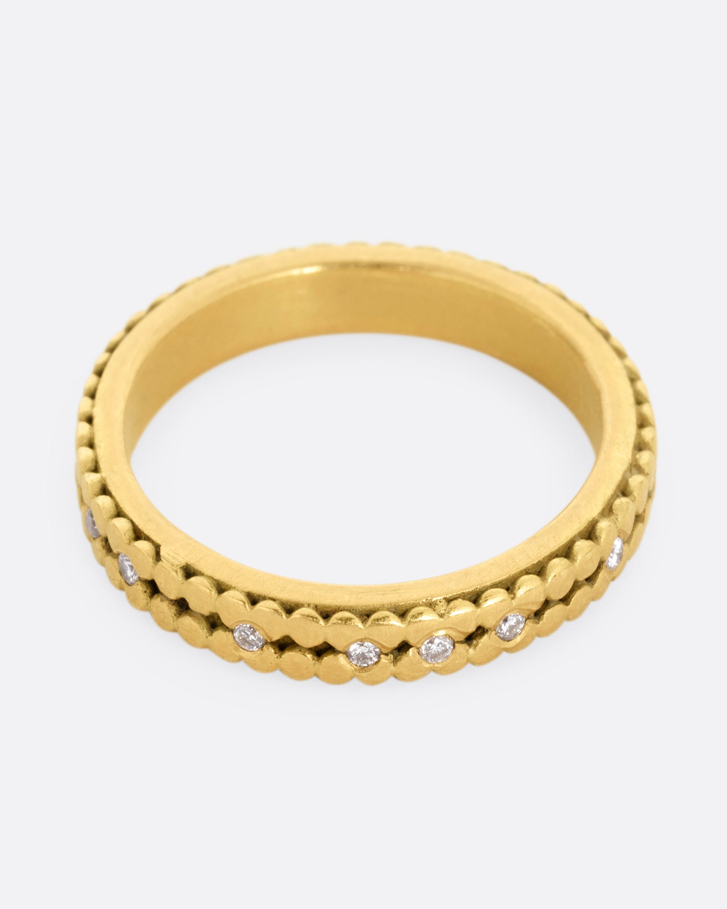 A yellow gold ring with two rows of dots and bezel set diamonds peppered along the center line. Shown from the top.