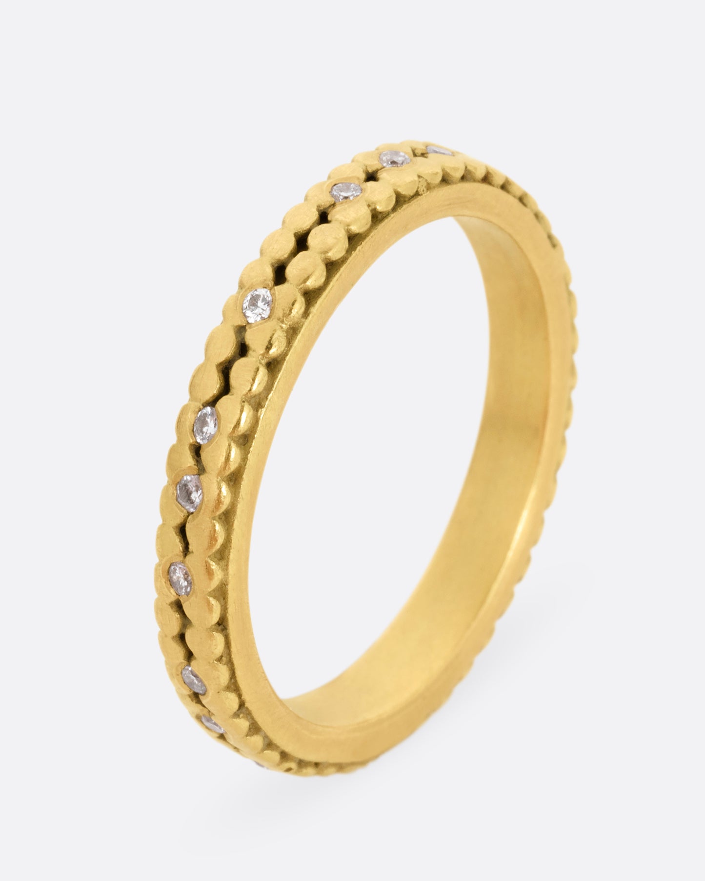 A yellow gold ring with two rows of dots and bezel set diamonds peppered along the center line. Shown standing up from the side.