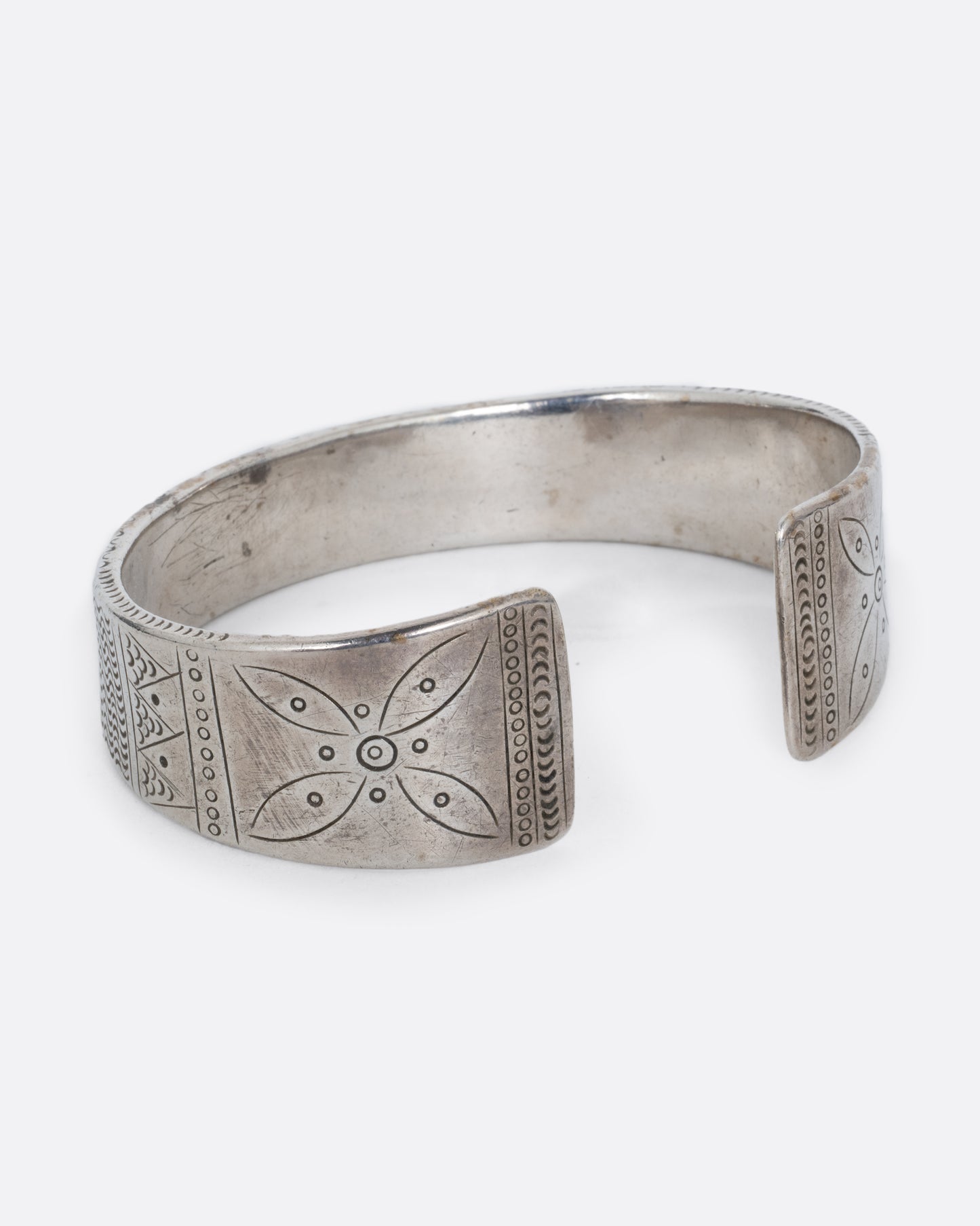 A silver bracelet with a graduated silhouette, hand stamped pattern, and opening in the front. Shown from the side.