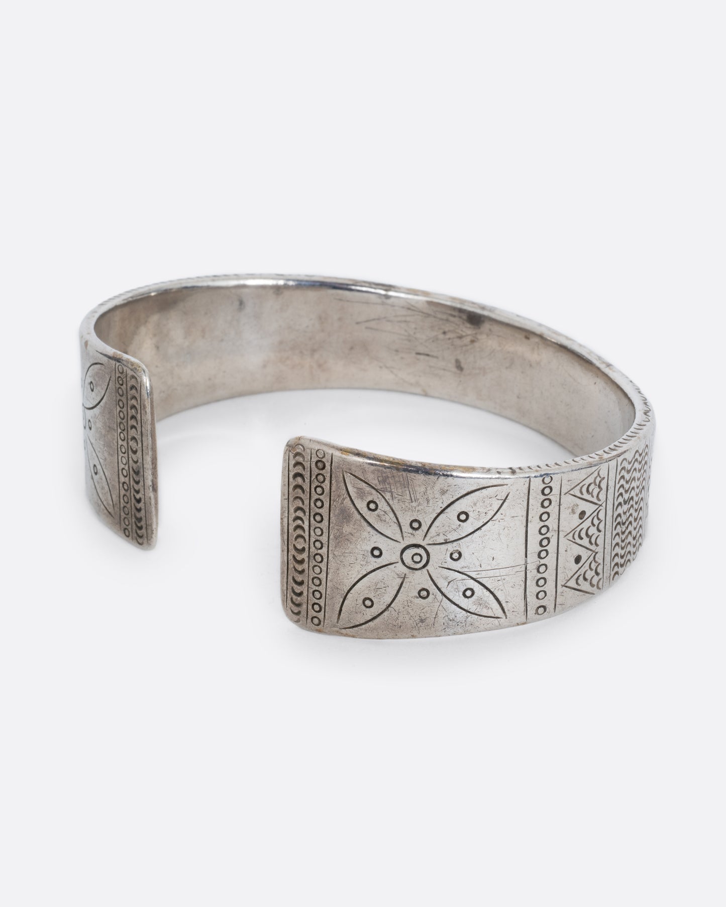 A silver bracelet with a graduated silhouette, hand stamped pattern, and opening in the front. Shown from the side.