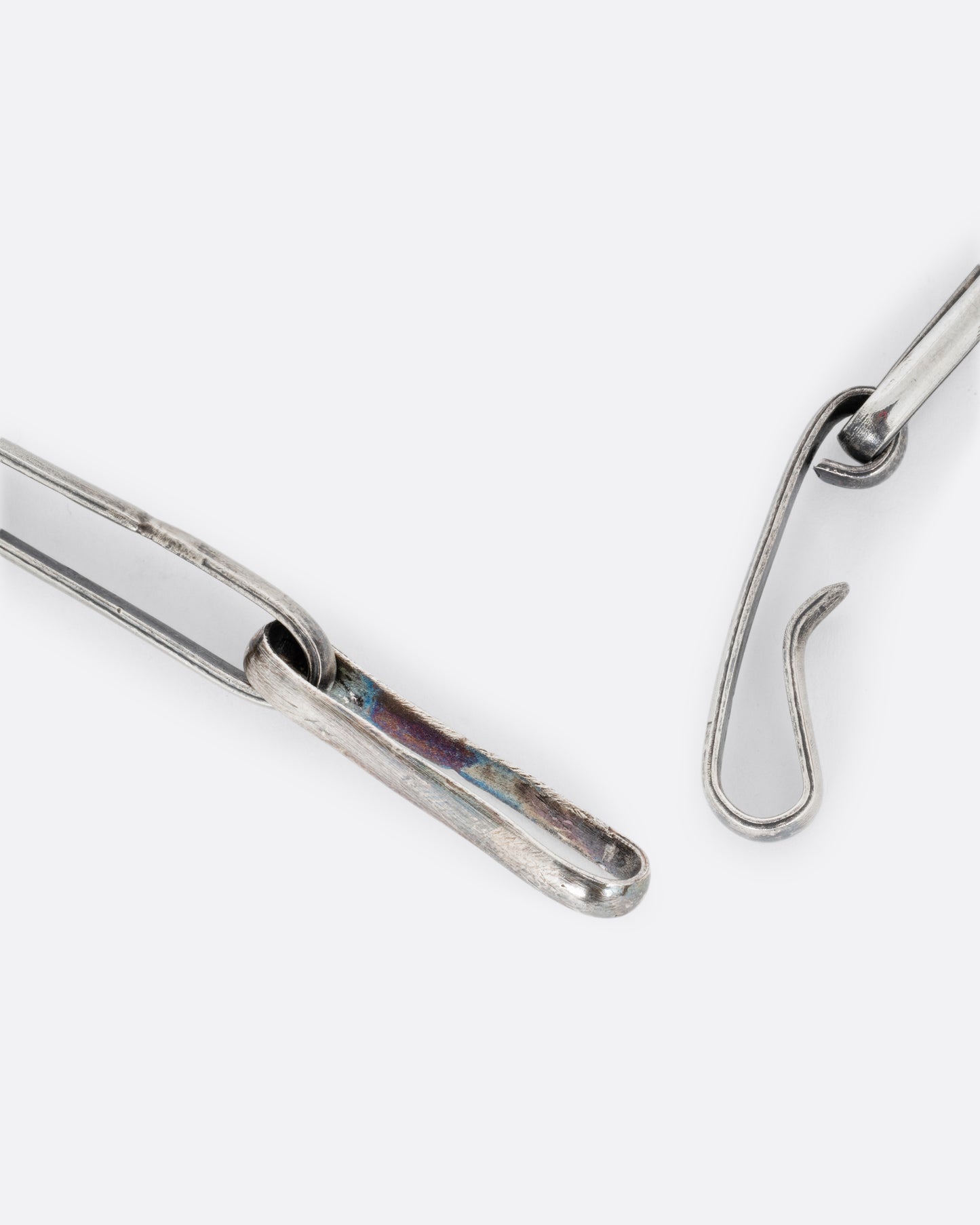 A close up of the clasp of a silver wide link cable chain necklace. Shown open.