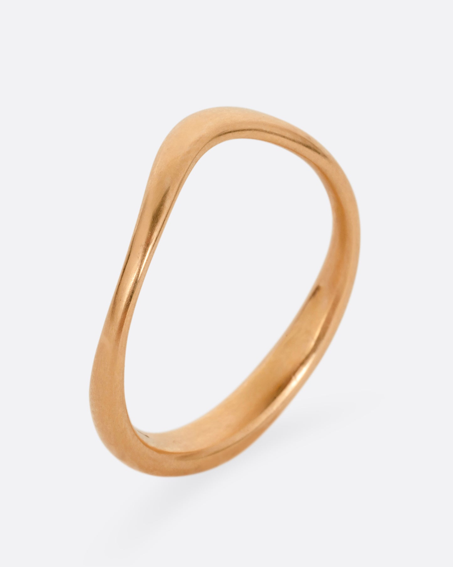 A rose gold ring with a gentle curve in the front. Shown standing up from the side.