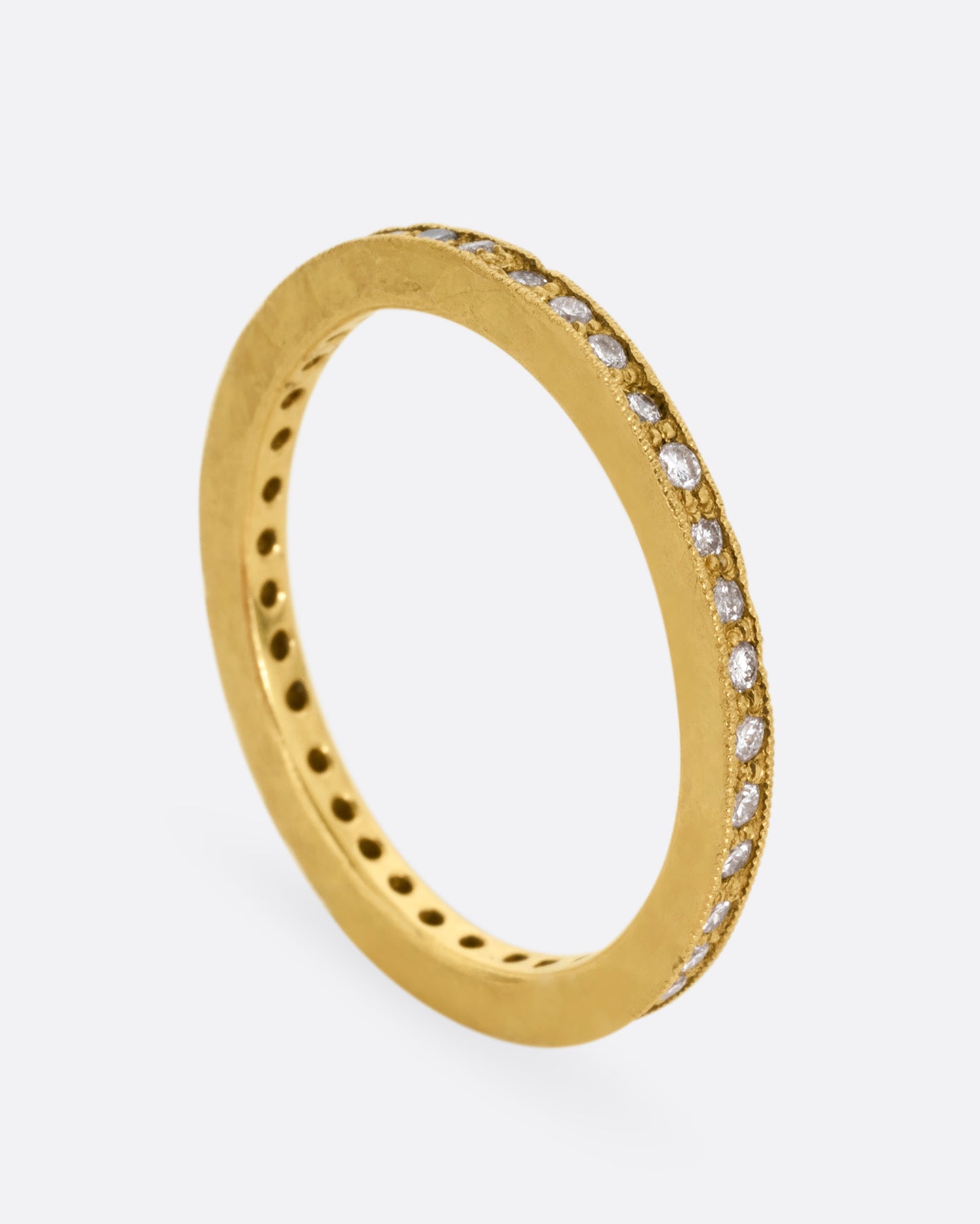 A yellow gold eternity band with bead set diamonds. Shown standing up from the side.