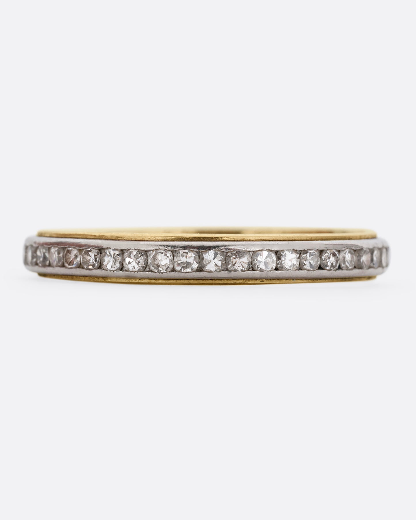 A platinum and yellow gold ring with channel set diamonds. Shown from the front.