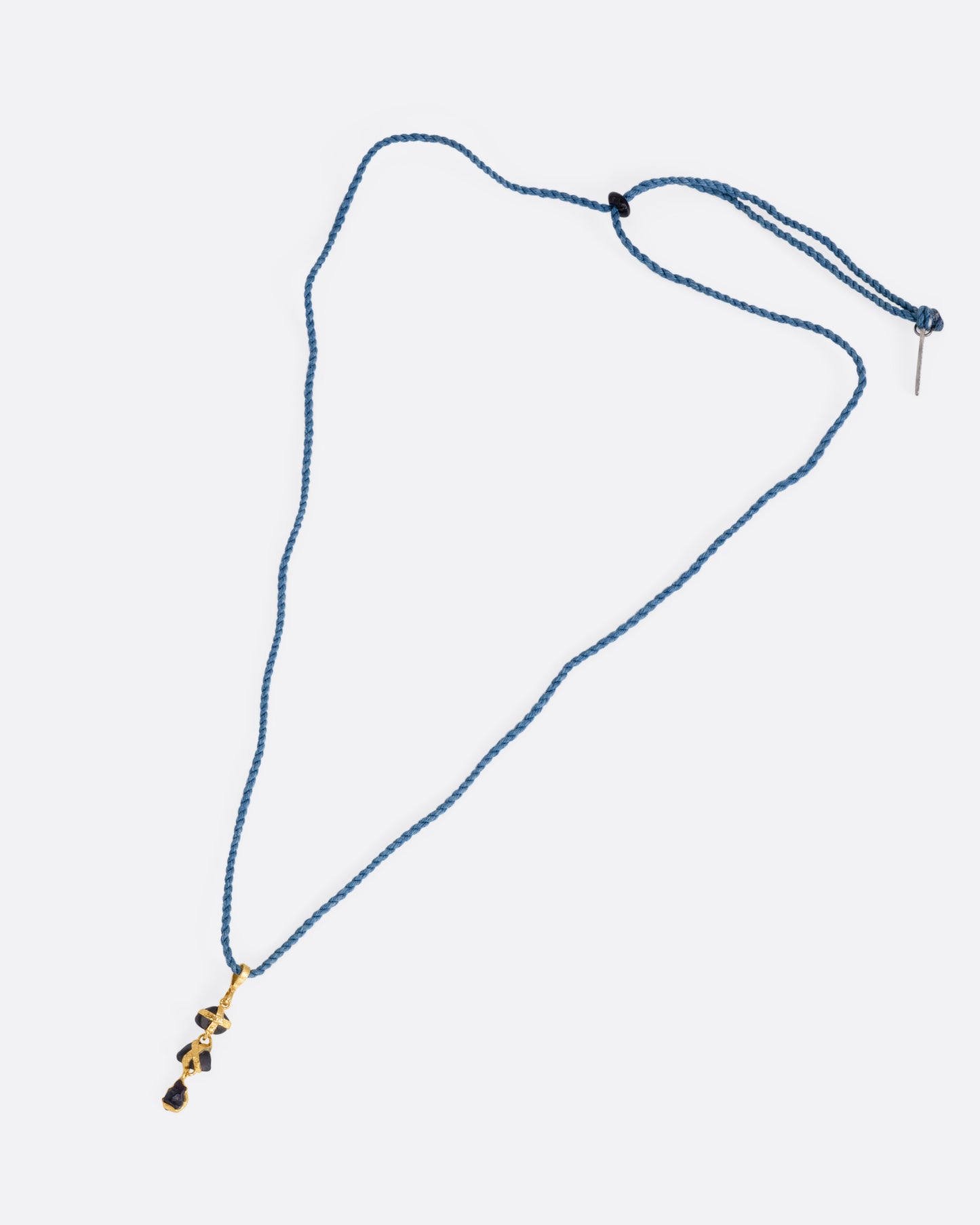 A yellow gold pendant with three raw sapphires on a cord, shown from the front.
