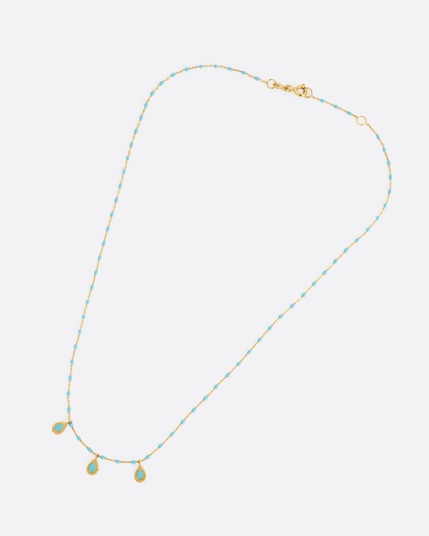 A yellow gold cable chain necklace with turquoise resin droplets along the chain and three teardrop shaped gold charms with turquoise resin centers. Shown closed from the front lying flat.
