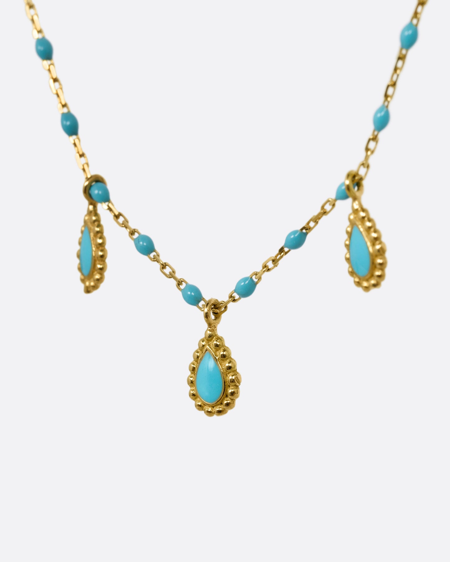 A yellow gold cable chain necklace with turquoise resin droplets along the chain and three teardrop shaped gold charms with turquoise resin centers. Shown from the side.