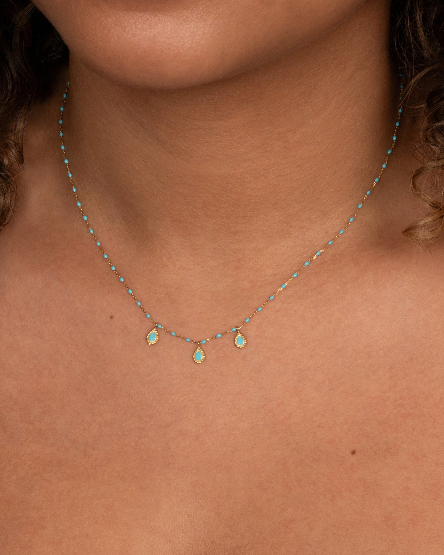 A yellow gold cable chain necklace with turquoise resin droplets along the chain and three teardrop shaped gold charms with turquoise resin centers. Shown from the front on a person.