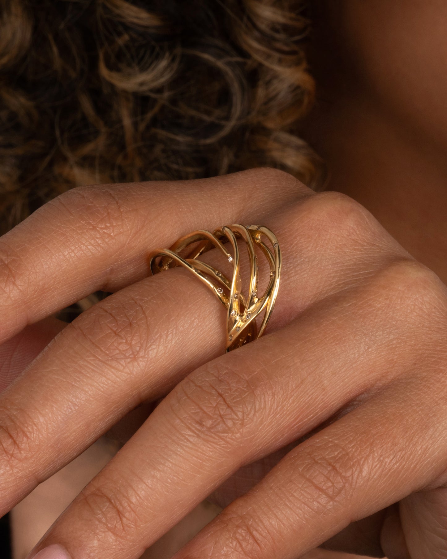 A yellow gold ring formed from multiple strands of gold, dotted with cognac diamonds. Shown on a hand.