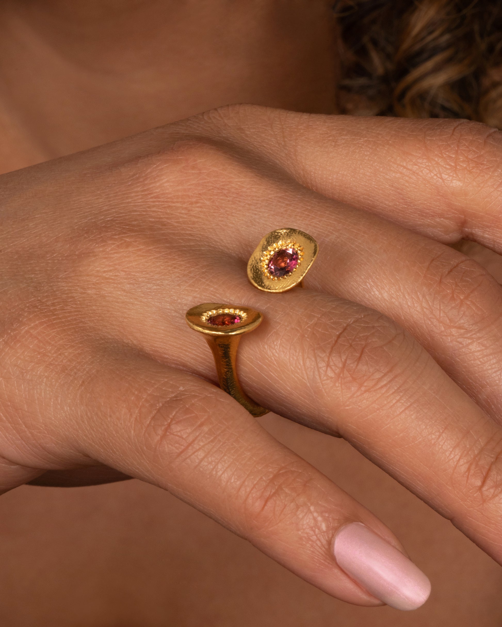 A high karat gold open ring with a large organic shaped disc on each end with a rosey pink tourmaline at its center. Shown on a hand.