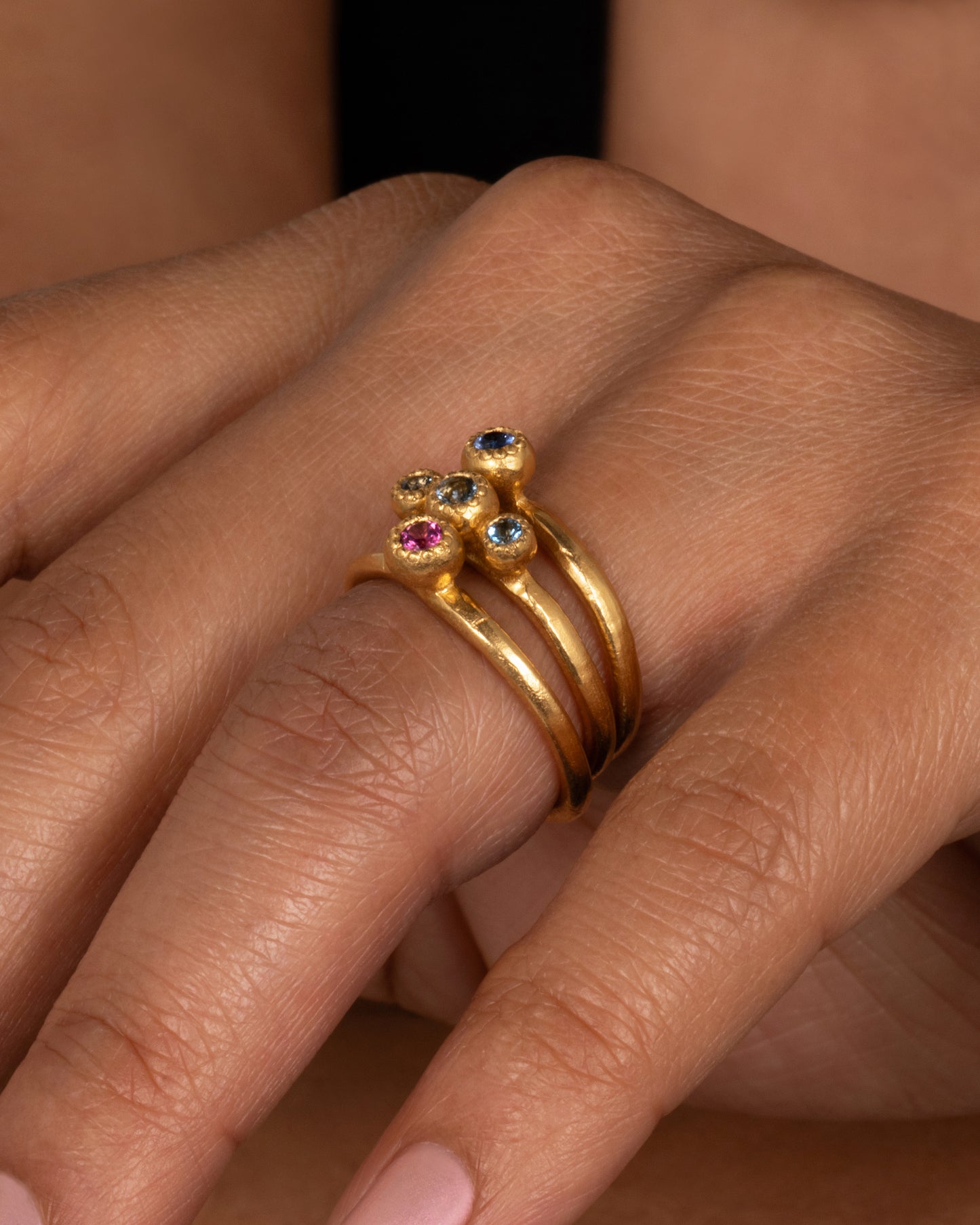 A high karat gold solitaire ring with a rosy pink tourmaline at its center. Shown on a finger.