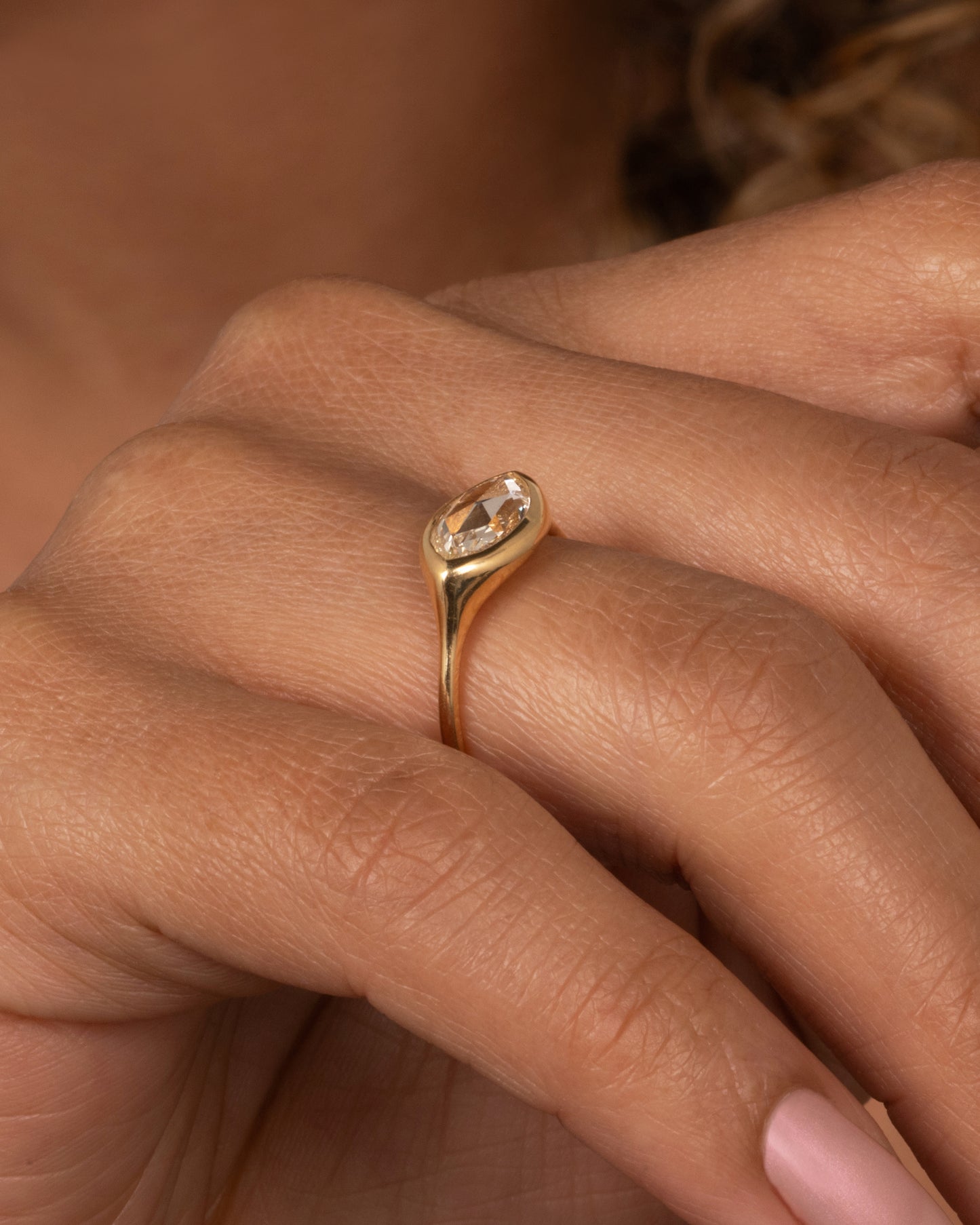 A yellow gold ring with a horizontal rose cut marquise diamond. Shown on a finger.