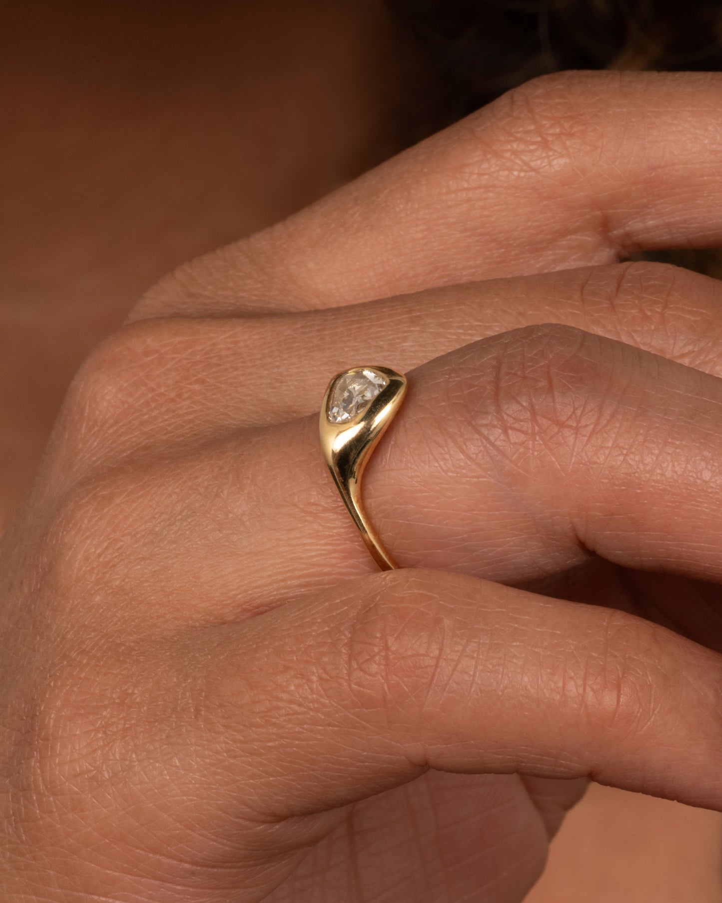 A yellow gold ring with a triangular rose cut diamond. Shown from the side on a finger.